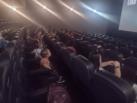 Crianças e acompanhantes sentados na sala de cinema, olhando para a tela