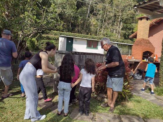 Crianças e adultos reunidos perto de um muro de pedra e uma churrasqueira de tijolos no quintal