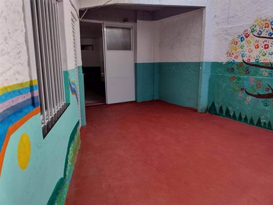 Pátio de entrada da creche, com piso vermelho e murais coloridos nas paredes