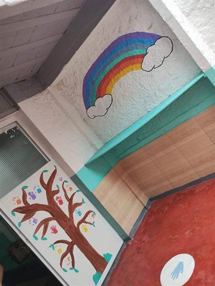 Porta com árvore de mãozinhas e parede com arco-íris na entrada do pátio