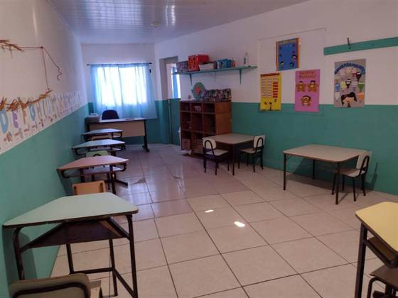 Sala de aula com carteiras, estante de brinquedos e cartazes de calendário e chamadinha