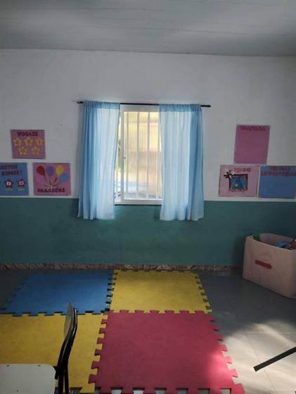 Cantinho com tapete de encaixe, janela com cortinas azuis e cartazes de vogais